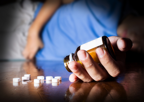 person laying on ground with pills next to them